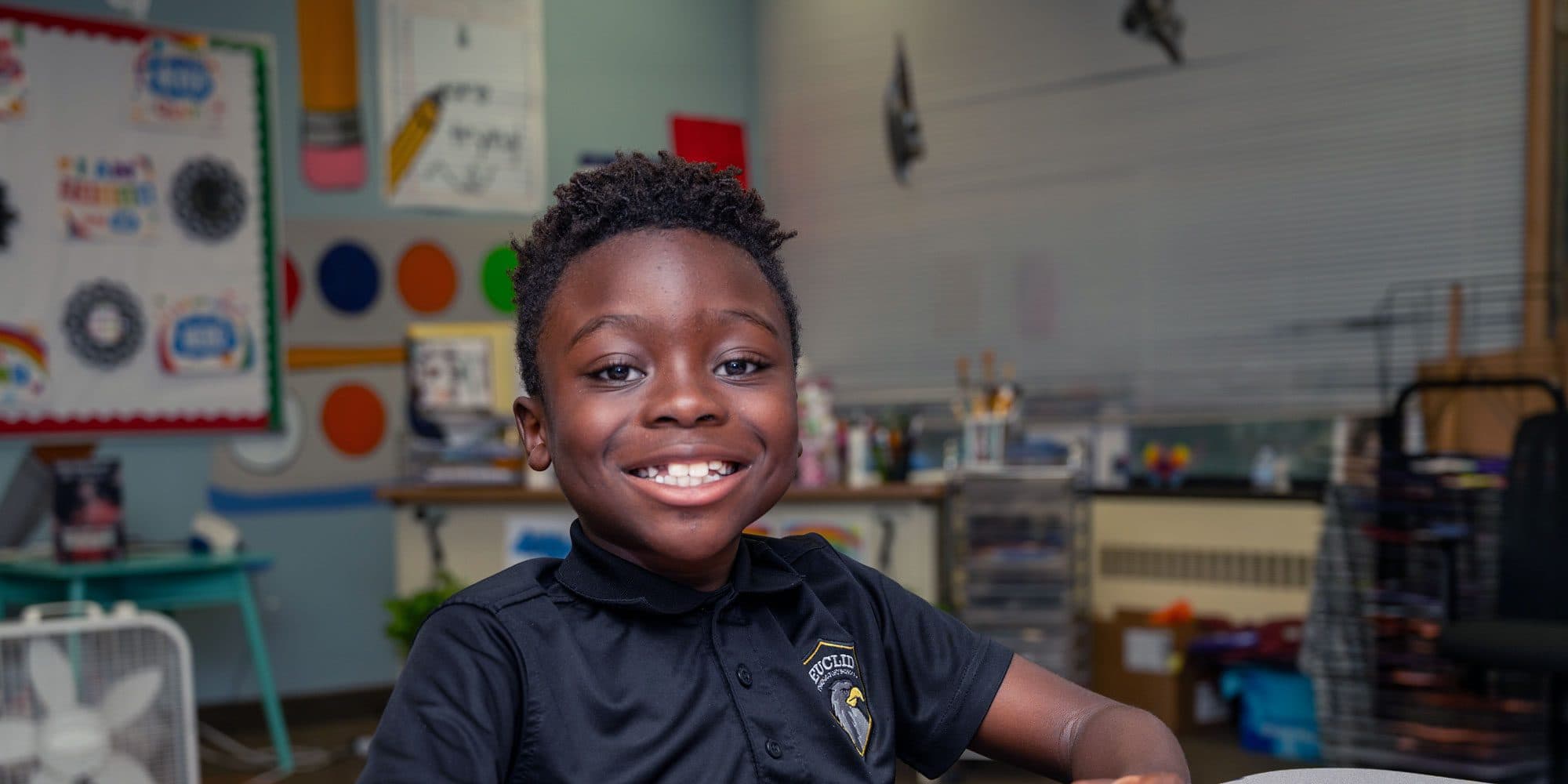 Smiling student in a Euclid Prep polo sits in a classroom.