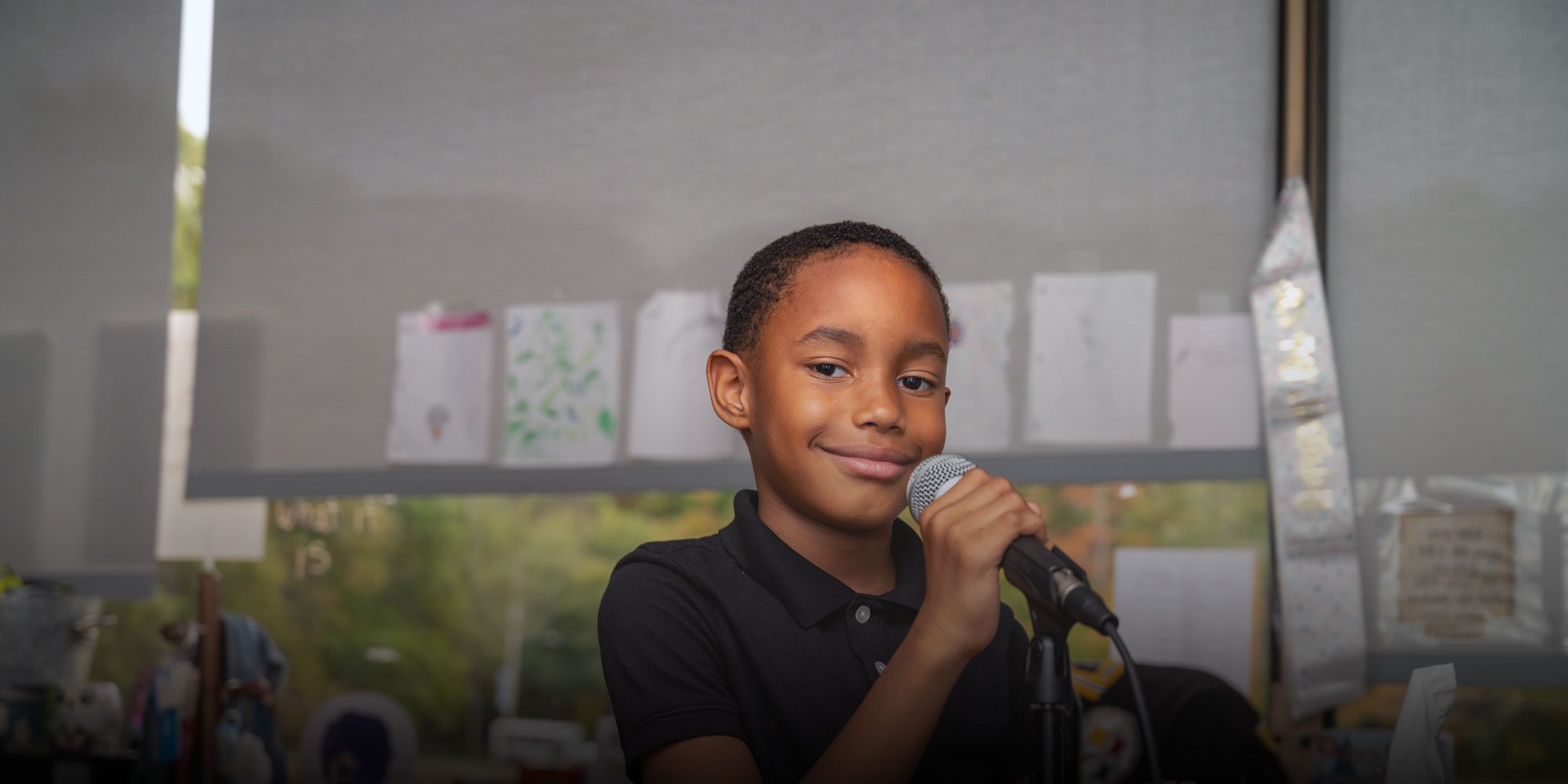 Student in a black polo smiles while speaking into a microphone.